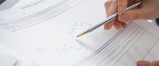 Eine Hand zeigt mit einem Stift auf ein Diagramm zur Bestimmung der fruchtbaren Tage.