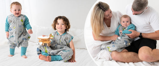 Links stehen und sitzen zwei Kinder in grauen Schlafsäcken mit blauen Ärmeln und Beinen auf einem weißen Bett. Eines der Kinder hält ein Spielzeugflugzeug.