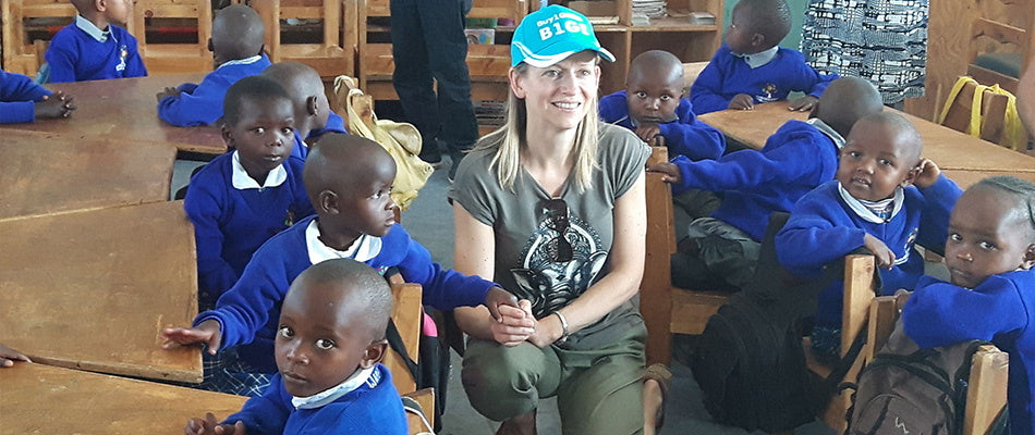 Eine Frau sitzt inmitten einer Gruppe von Kindern in einem Klassenzimmer. Die Kinder tragen blaue Schuluniformen.