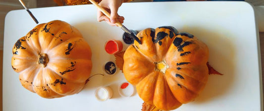 Kinder bemalen zwei Kürbisse mit schwarzen und roten Farben für Halloween.