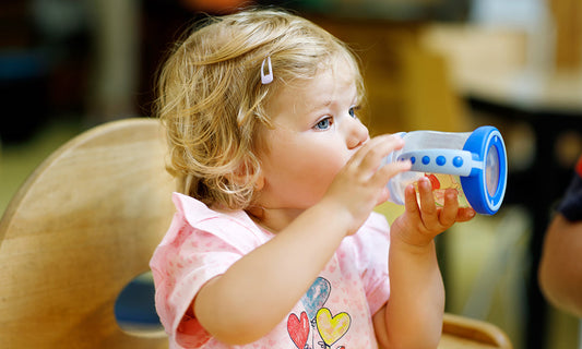 Kleinkind sitzt im Hochstuhl und trinkt Wasser aus einer Flasche
