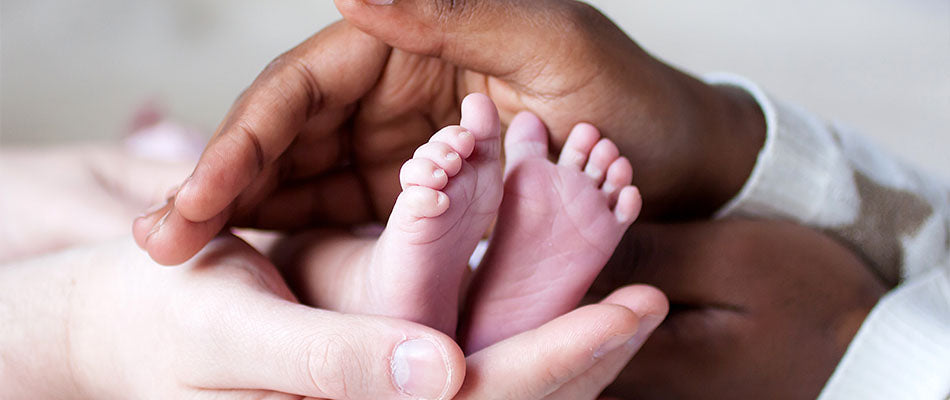Elternhände umschließen sanft die Füße eines neugeborenen Babys.