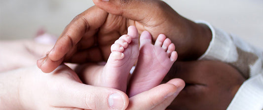 Elternhände umschließen sanft die Füße eines neugeborenen Babys.