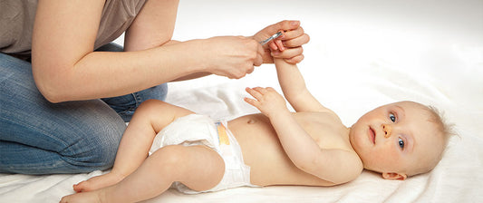 Eine Person schneidet einem Baby, das nur eine Windel trägt, die Fingernägel.