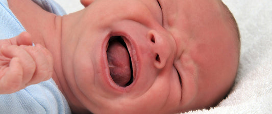 Ein weinendes Baby in Nahaufnahme auf einem weißen Hintergrund liegend.