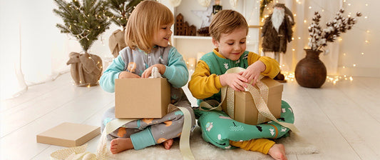 Zwei Kinder öffnen Weihnachtsgeschenke vor einem geschmückten Baum in festlicher Umgebung.