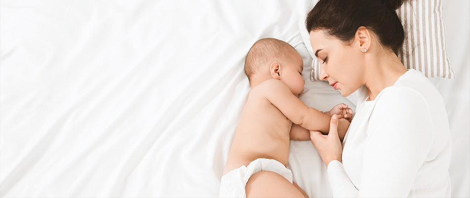Mutter und Baby schlafen eng aneinander gekuschelt auf einem weißen Bett.