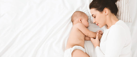 Mutter und Baby schlafen eng aneinander gekuschelt auf einem weißen Bett.